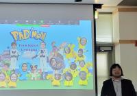 Ice stands beside a projection screen displaying an illustration titled "PhD-mon: Team Rocket  Pikachus" depicting the research groups of Zalatan and Carothers as Pokemon.